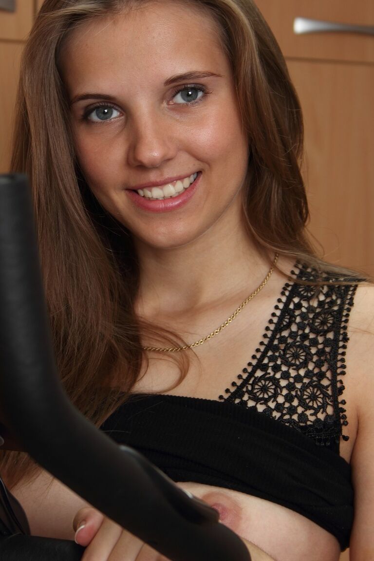 21P Small titted teen with a slim figure Kira strips and poses on an exercise bike