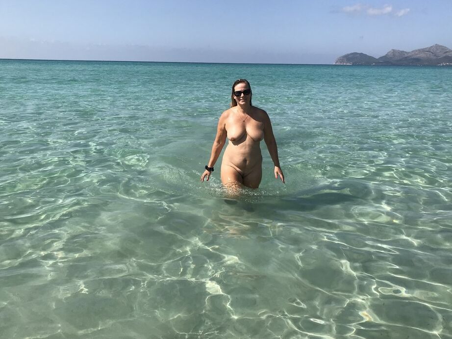 20P Middle-aged woman wears shades while totally naked in the ocean