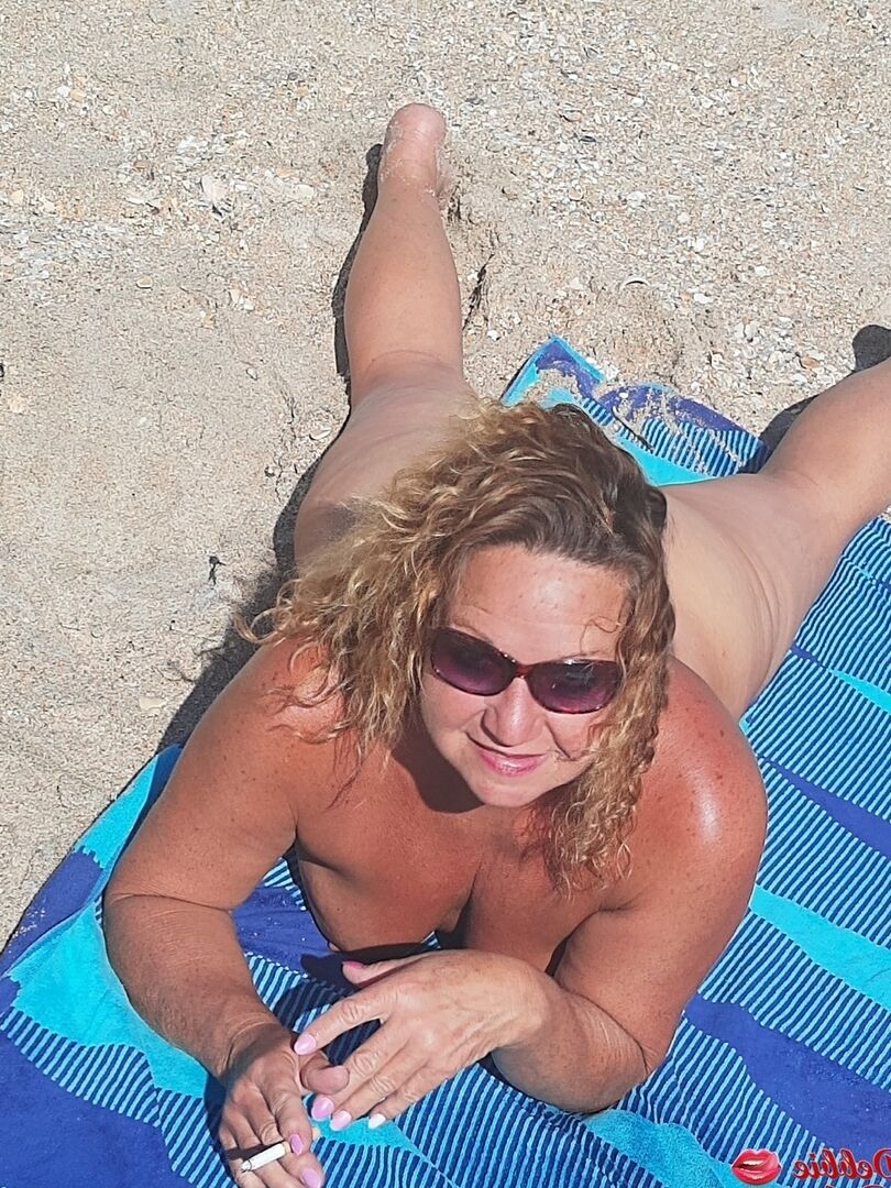 16P Debbie Delicious, amatrice plus âgée, fume en prenant un bain de soleil nue sur une plage