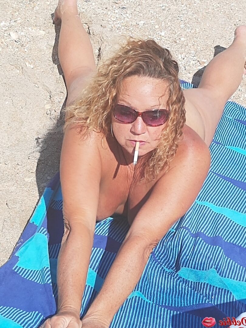 16P Debbie Delicious, amatrice plus âgée, fume en prenant un bain de soleil nue sur une plage