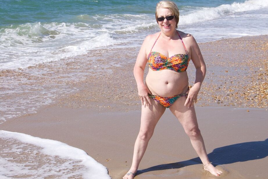20P Mature UK woman Speedy Bee wears sunglasses while getting naked at the beach