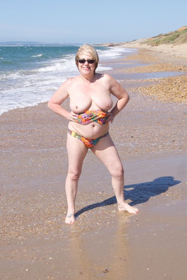 20P Mature UK woman Speedy Bee wears sunglasses while getting naked at the beach