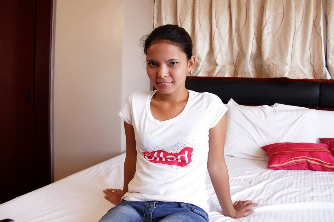 Asiatischer 12-Jähriger zieht vor dem Sex auf weißen Bettlaken ein T-Shirt und blaue Jeans aus