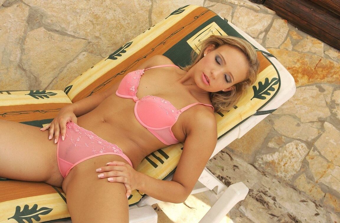 18P Chica rubia caliente se quita su conjunto de lencería rosa en un sillón en el patio