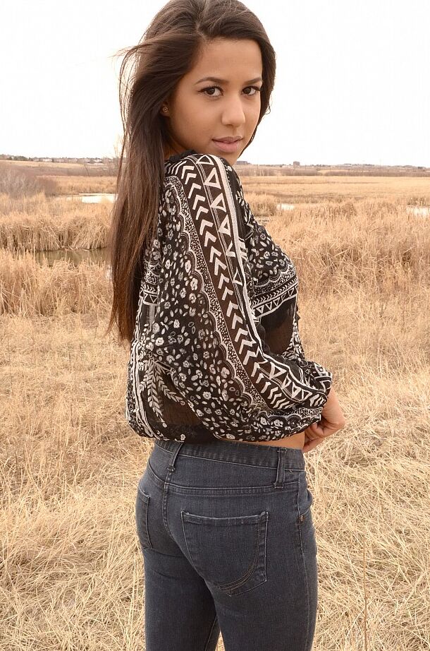 12P A garota latina Bella Quinn modela em um campo usando sutiã e jeans