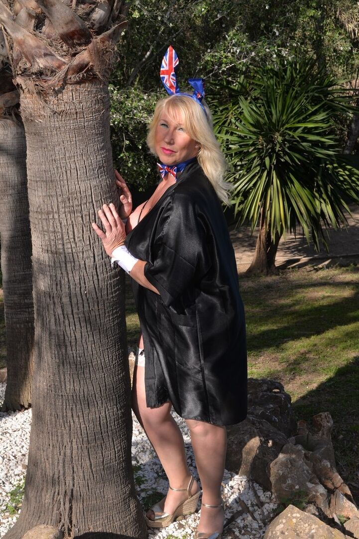 16P Melody, une grosse blonde plus âgée, joue avec ses énormes seins à côté d'un arbre.