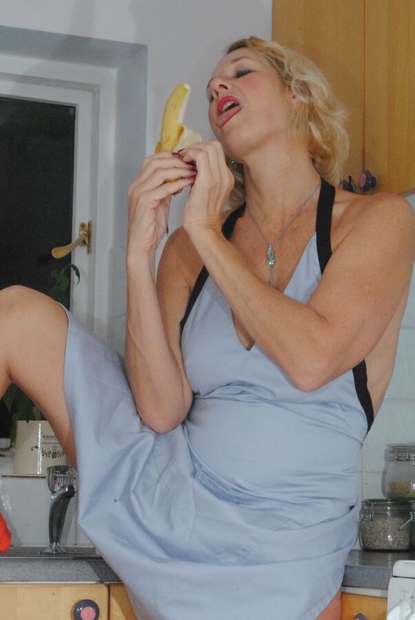 19P Mature MILF with blonde hair wears only an apron while devouring a banana