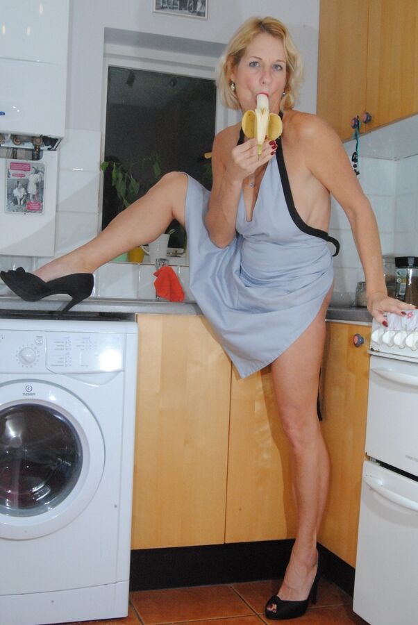 19P Mature MILF with blonde hair wears only an apron while devouring a banana