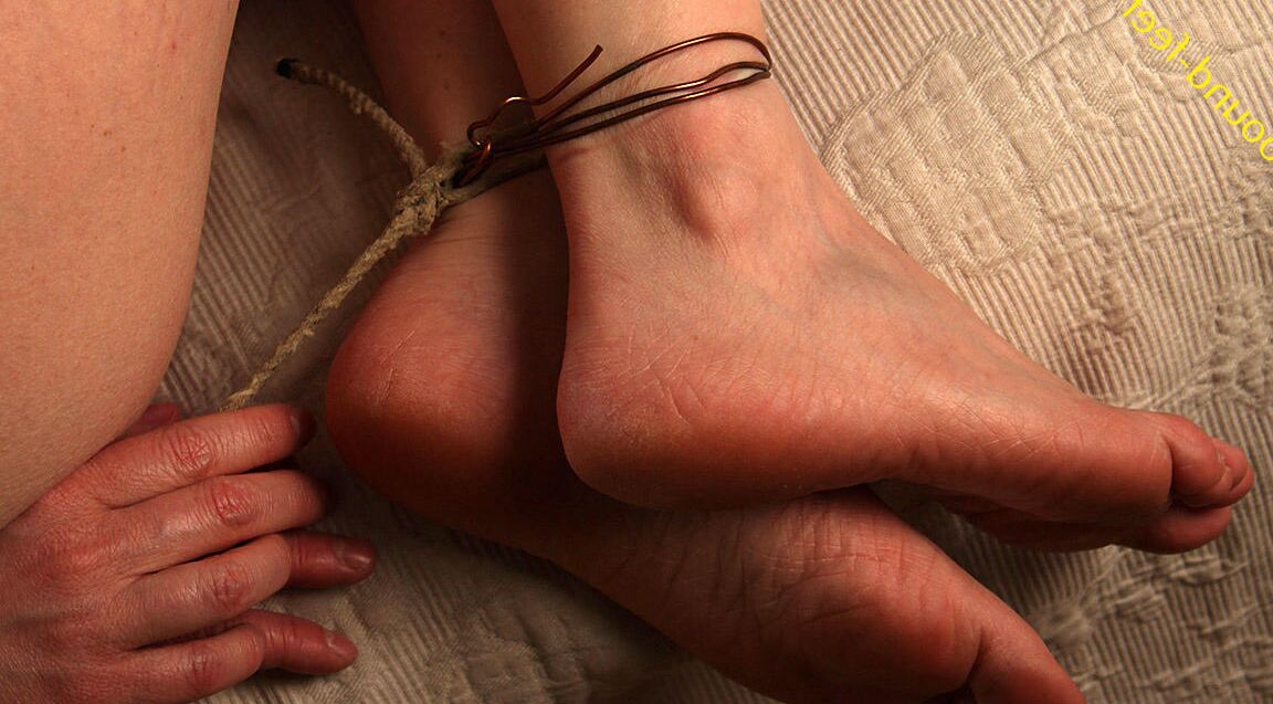 16P Caucasian girl is hogtied with wire in a black corset on a bed