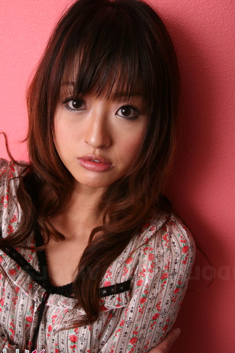15P Japanese model with a pretty face stands clothed against a pink wall