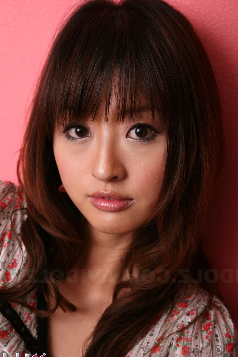 15P Japanese model with a pretty face stands clothed against a pink wall