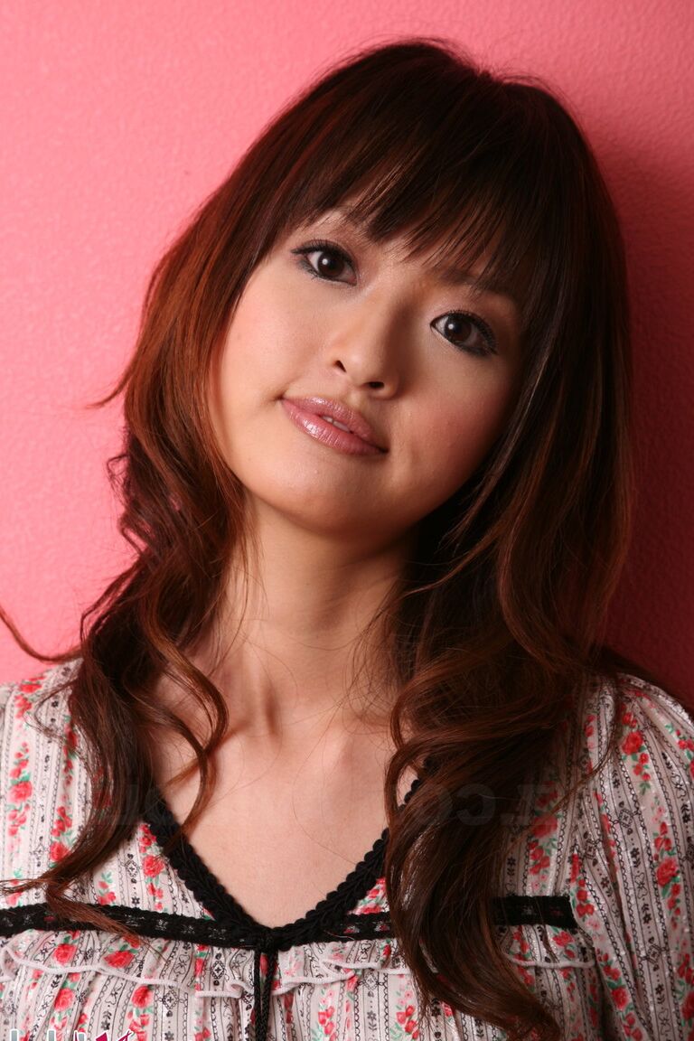 15P Japanese model with a pretty face stands clothed against a pink wall