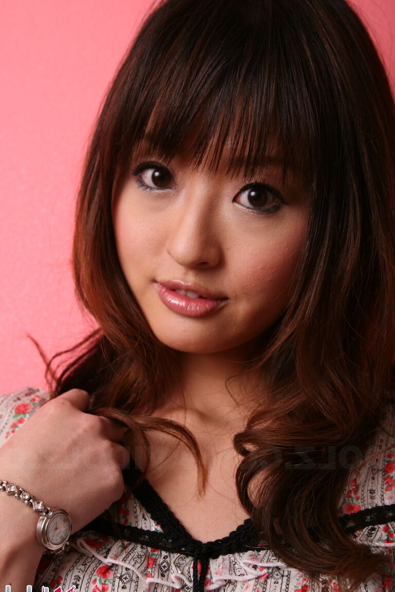 15P Japanese model with a pretty face stands clothed against a pink wall