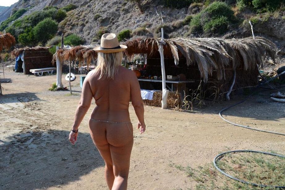 18P Dicke blonde Frau mit großen Brüsten wandert mit Strohhut an einem FKK-Strand entlang