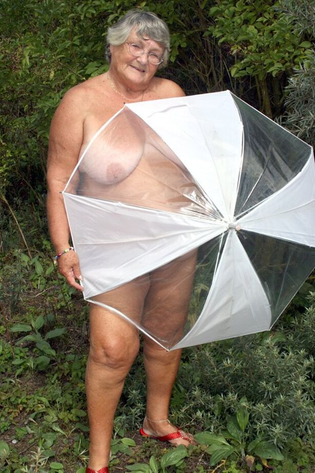 20P Obese oma Grandma Libby holds an umbrella while posing naked by fir trees
