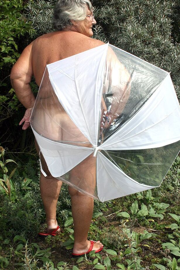 20P Obese oma Grandma Libby holds an umbrella while posing naked by fir trees