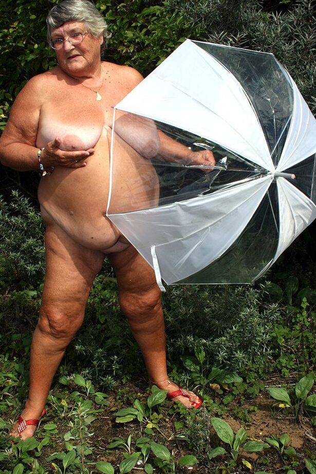 20P Obese oma Grandma Libby holds an umbrella while posing naked by fir trees
