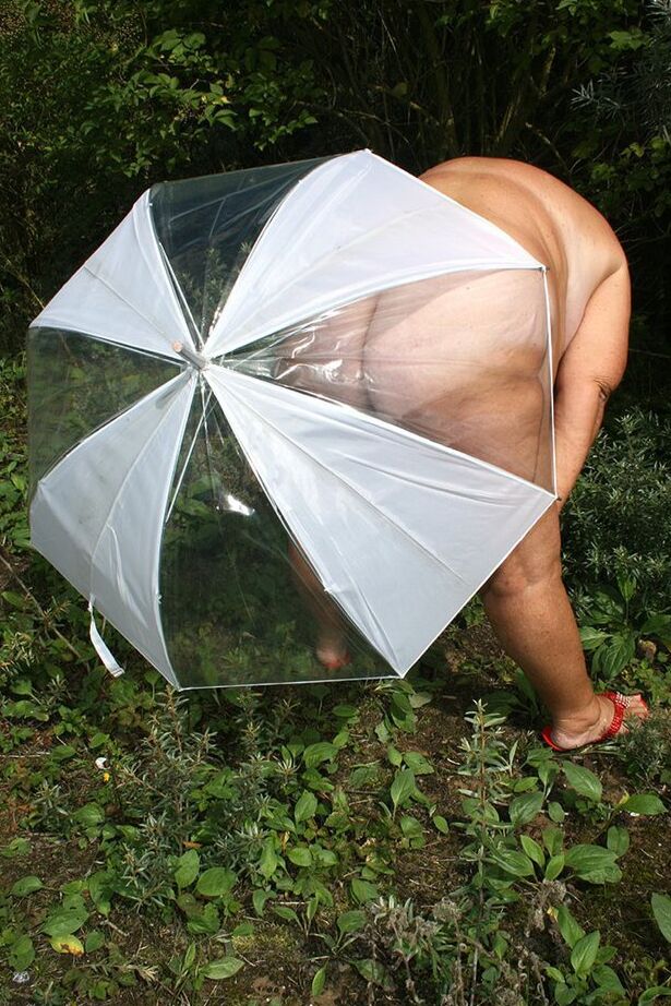 20P Obese oma Grandma Libby holds an umbrella while posing naked by fir trees
