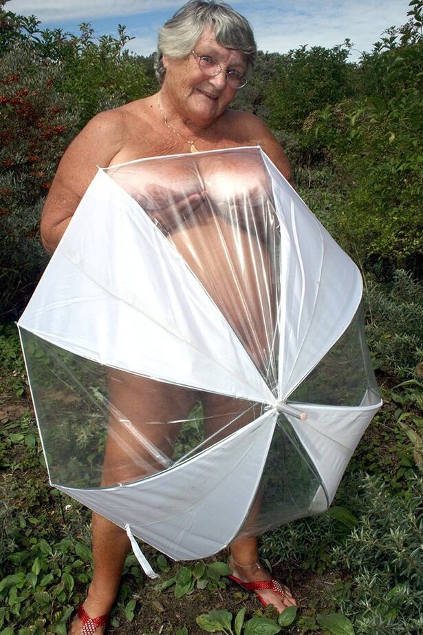 20P Obese oma Grandma Libby holds an umbrella while posing naked by fir trees