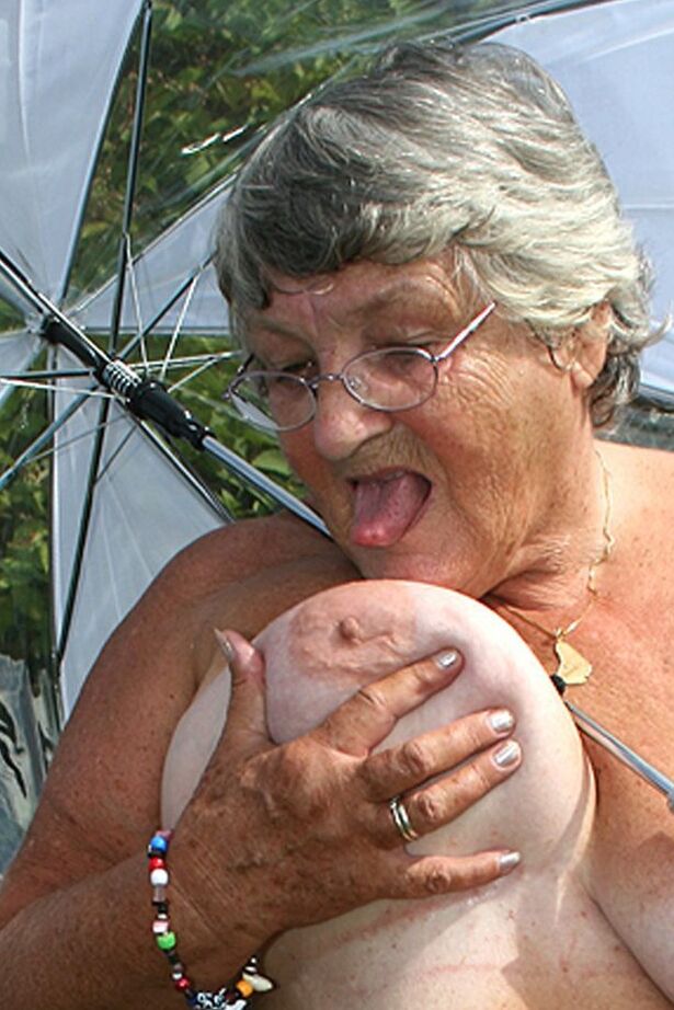 20P Obese oma Grandma Libby holds an umbrella while posing naked by fir trees