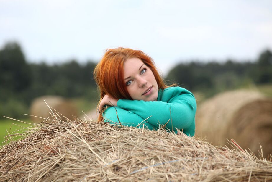 16P Amber A, rousse naturelle, pose son corps d'adolescente nue sur une botte ronde de foin.