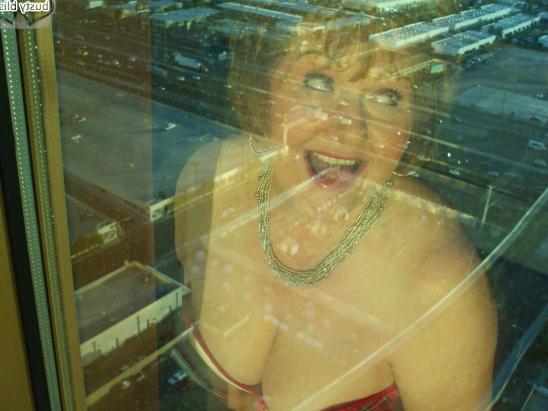 20P Reife Frau Busty Bliss lässt ihre großen Titten aus einem Korsett am Fenster ihrer Wohnung fallen