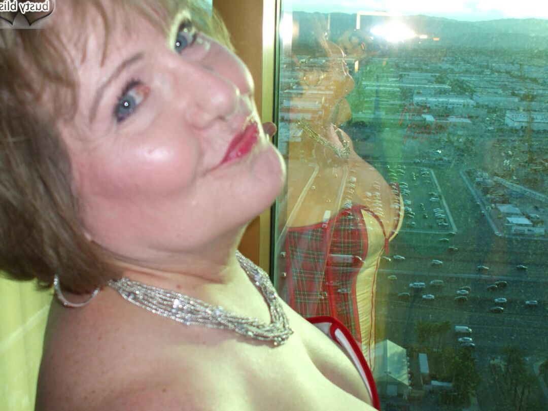 20P Reife Frau Busty Bliss lässt ihre großen Titten aus einem Korsett am Fenster ihrer Wohnung fallen