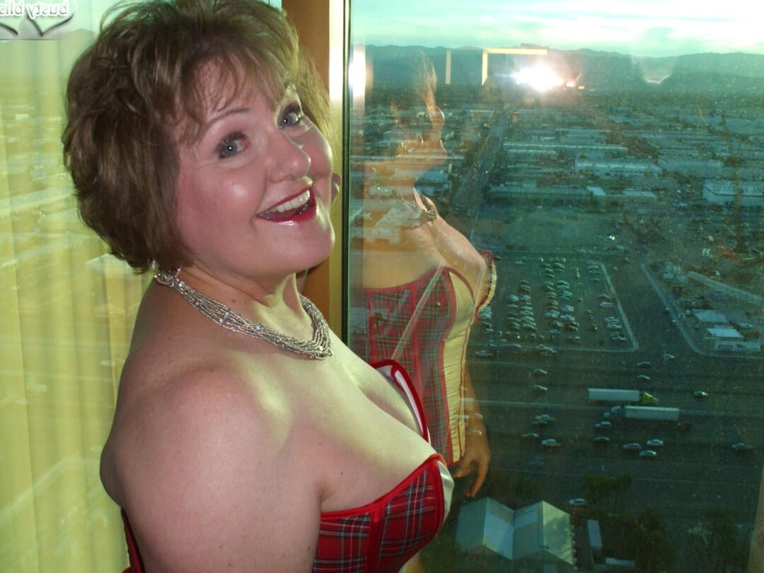 20P Reife Frau Busty Bliss lässt ihre großen Titten aus einem Korsett am Fenster ihrer Wohnung fallen