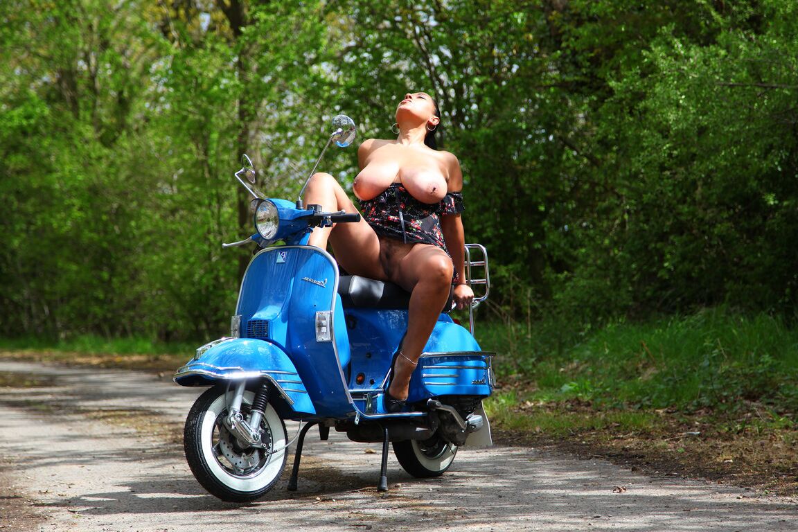 21P Danica Collins, une MILF bien roulée, montre ses seins géants sur une moto dans les bois.