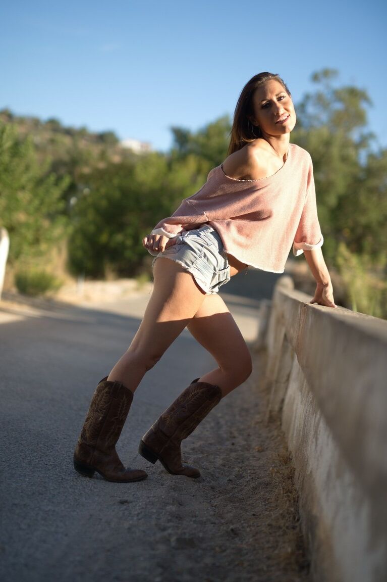 12P Solo model Jess West walks along a road in nothing more than her cowgirl boots