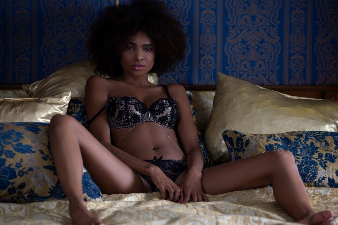 12P Ebony centerfold model Bruna Rocha poses topless in a thong upon a bed