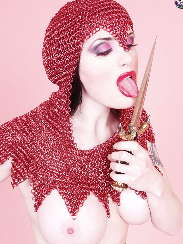 15P Busty chick Morrigan Hel licks a dagger while wearing chain mail and OTK boots