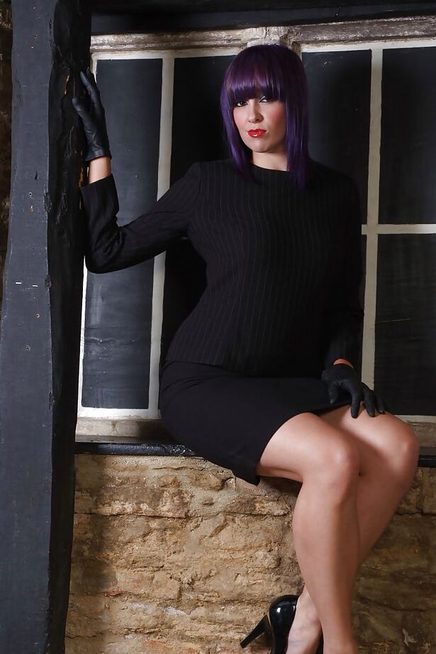 15P Chica guapa con cabello morado posa completamente vestida con un vestido negro y zapatos de tacón