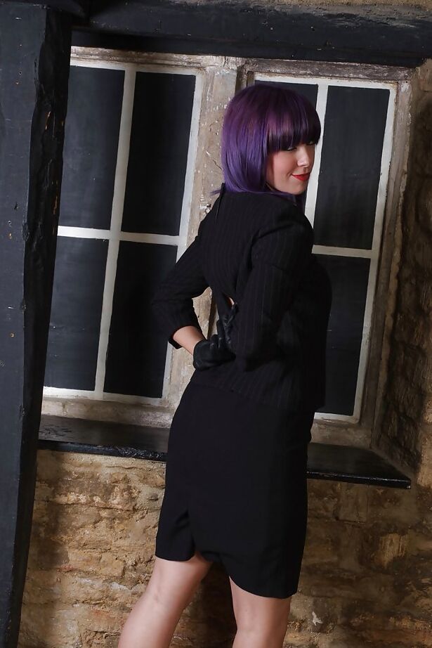 15P Chica guapa con cabello morado posa completamente vestida con un vestido negro y zapatos de tacón