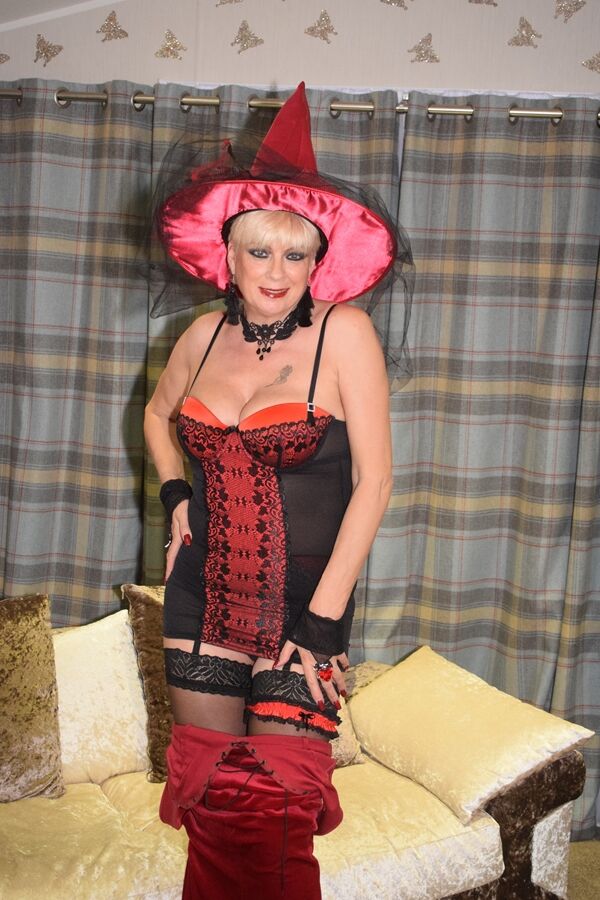 20P Rubia mayor se quita un vestido de terciopelo rojo y posa desnuda con un sombrero de bruja y medias