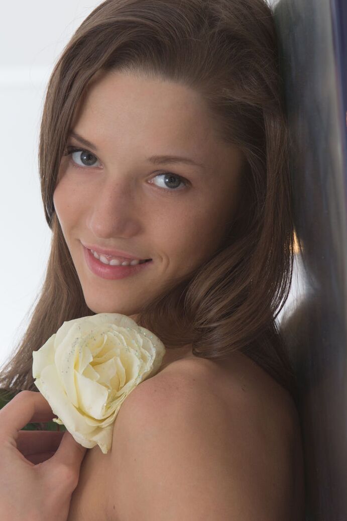 20P La jeune brune Britney tient une rose blanche alors qu'elle se déshabille totalement sur un lit.