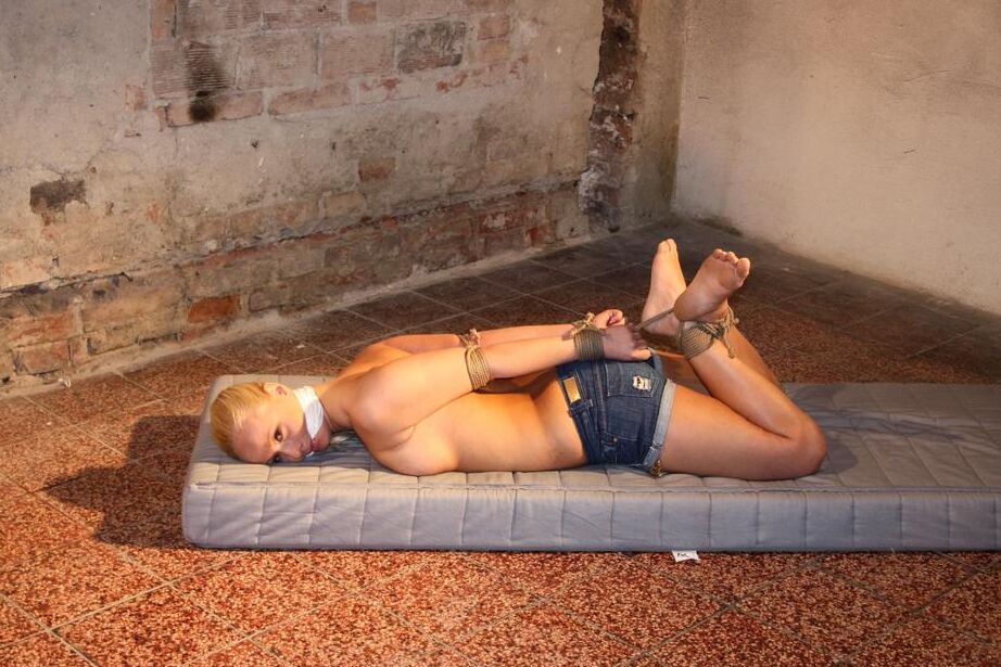 16P Blonde female with a high ponytail is left gagged and hogtied on a mattress