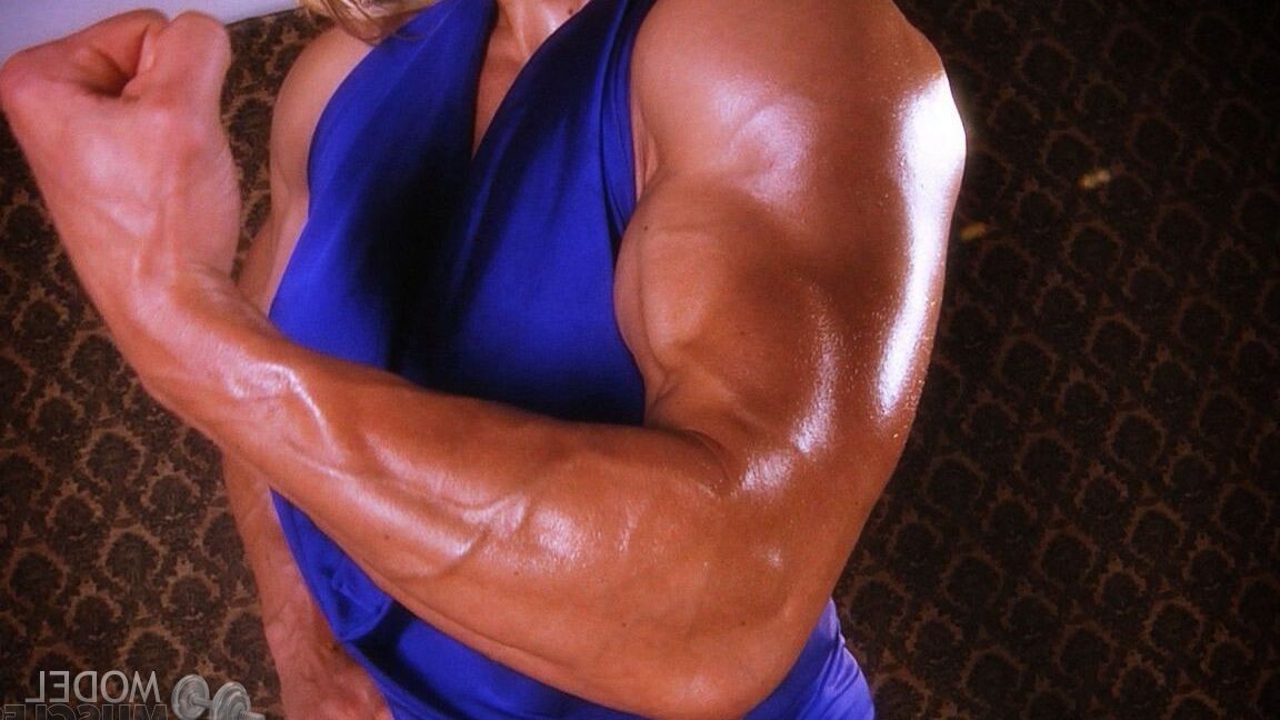 21P La culturista madura Brigita Brezovac flexionando sus grandes músculos con un vestido azul