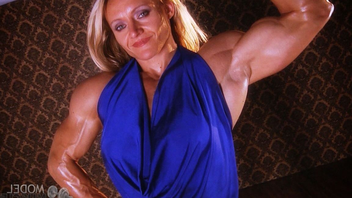 21P La culturista madura Brigita Brezovac flexionando sus grandes músculos con un vestido azul