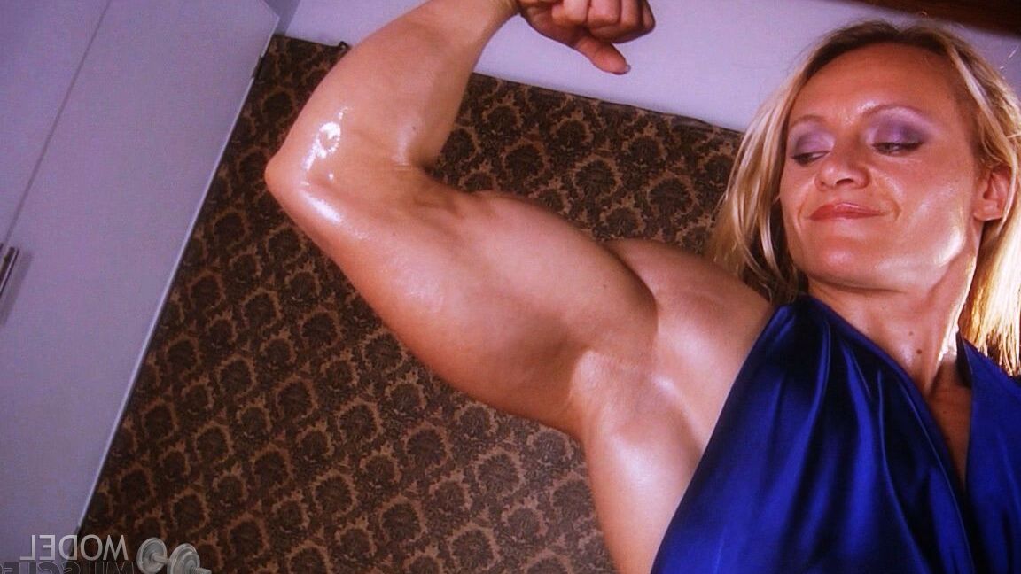 21P La culturista madura Brigita Brezovac flexionando sus grandes músculos con un vestido azul