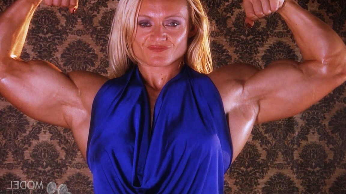 21P La culturista madura Brigita Brezovac flexionando sus grandes músculos con un vestido azul