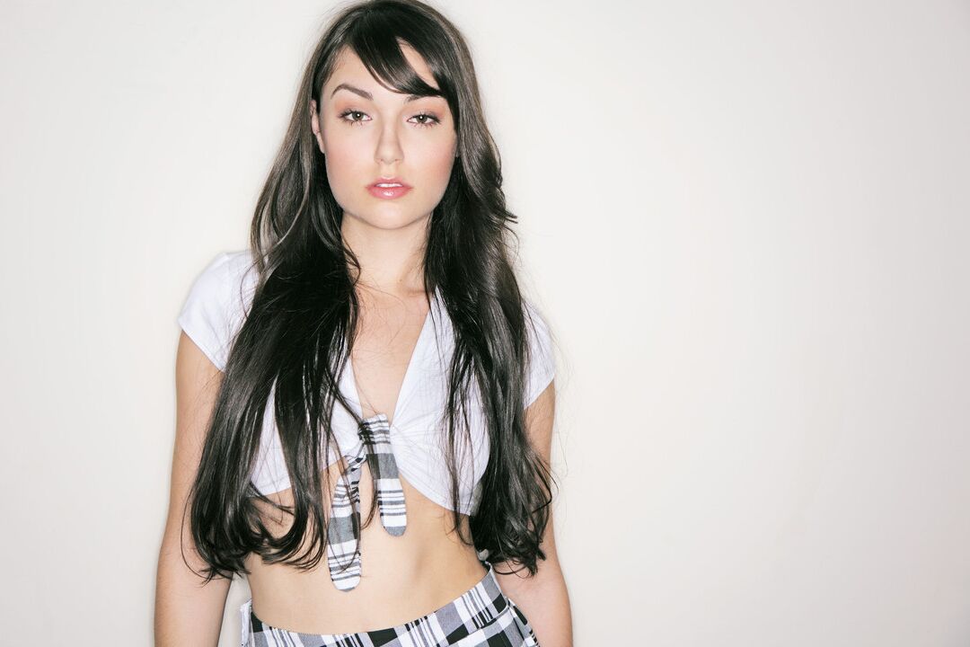 Le modèle 16P Solo Sasha Grey enlève son haut avec une jupe plissée et des bas.