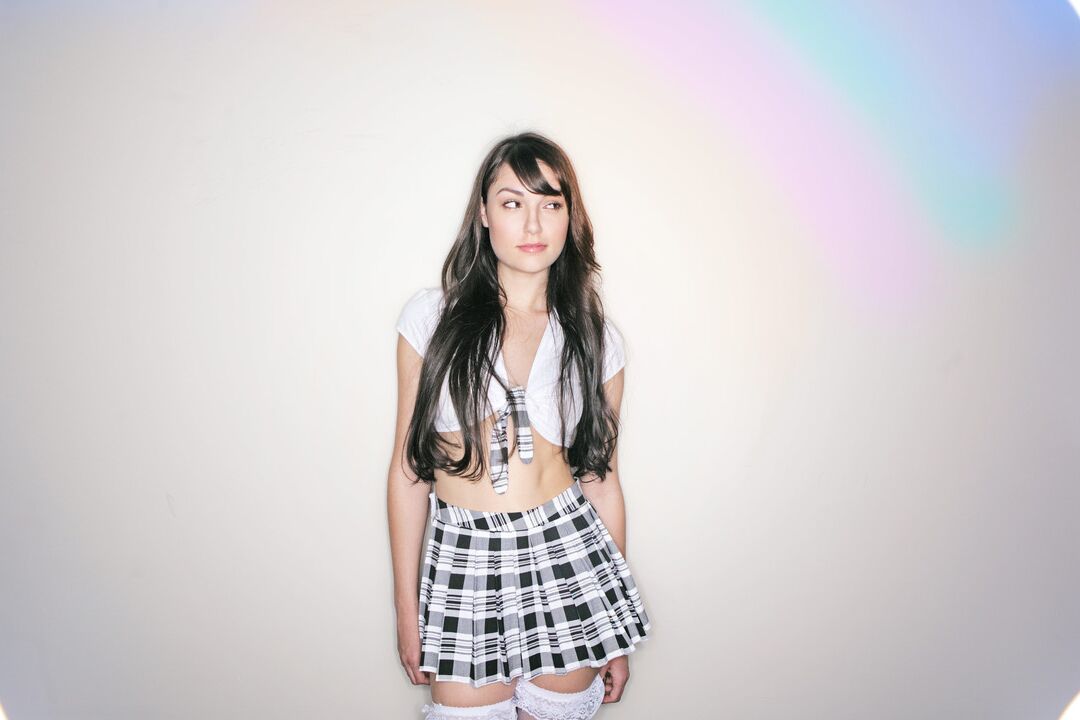 Le modèle 16P Solo Sasha Grey enlève son haut avec une jupe plissée et des bas.
