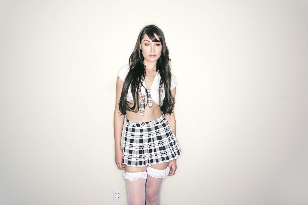 Le modèle 16P Solo Sasha Grey enlève son haut avec une jupe plissée et des bas.