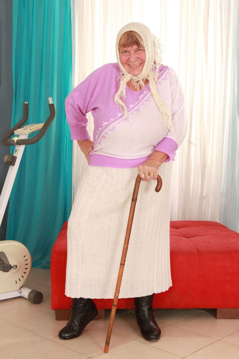 15P Old granny Sara G in skirt & boots sheds sweater to show huge tits in bra