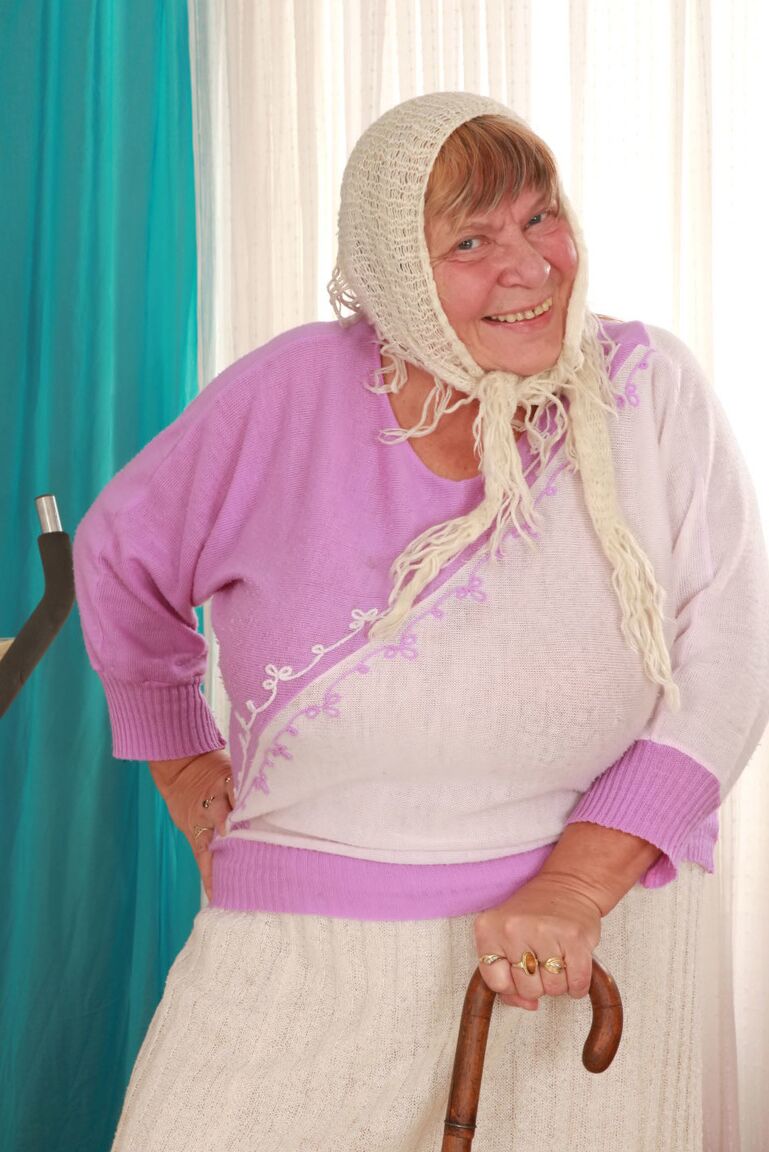 15P Old granny Sara G in skirt & boots sheds sweater to show huge tits in bra
