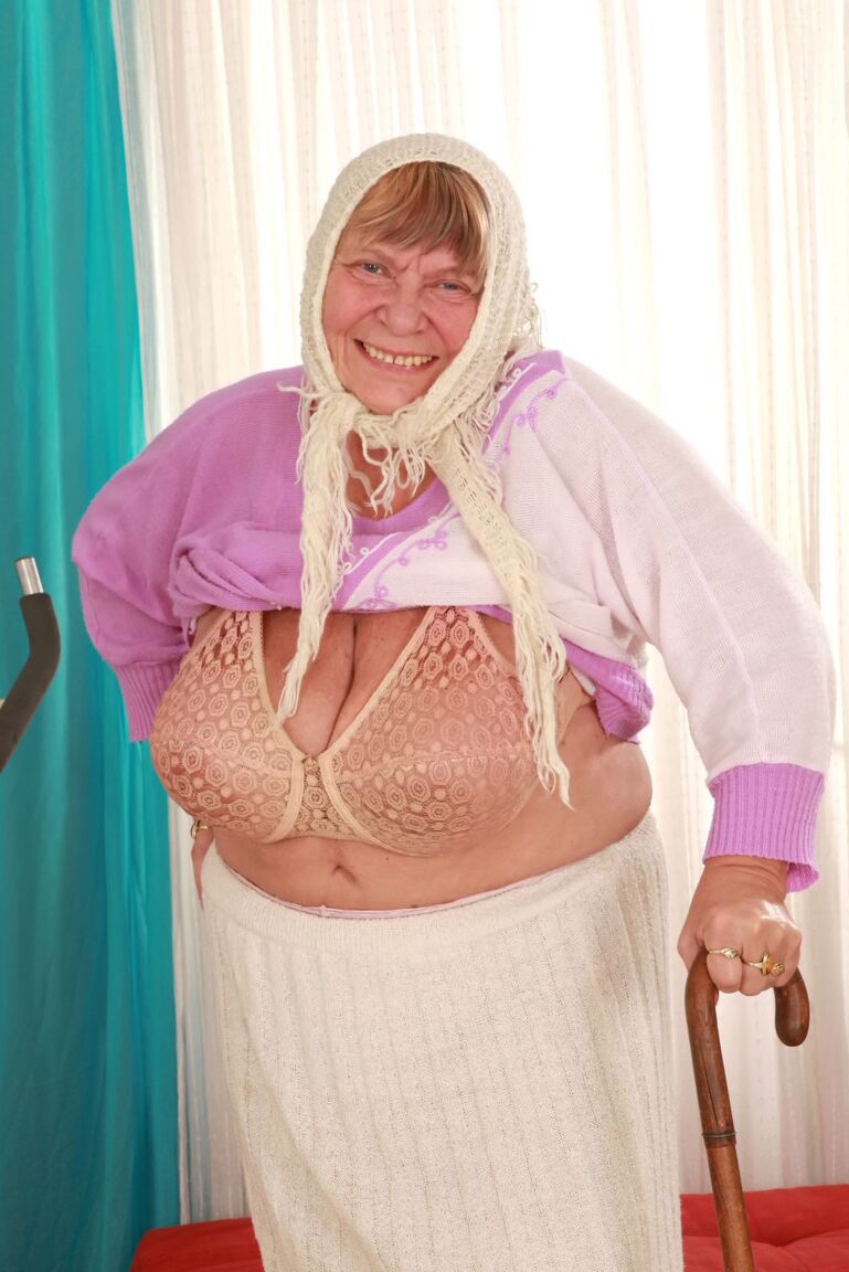 15P Old granny Sara G in skirt & boots sheds sweater to show huge tits in bra