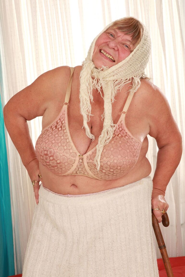 15P Old granny Sara G in skirt & boots sheds sweater to show huge tits in bra