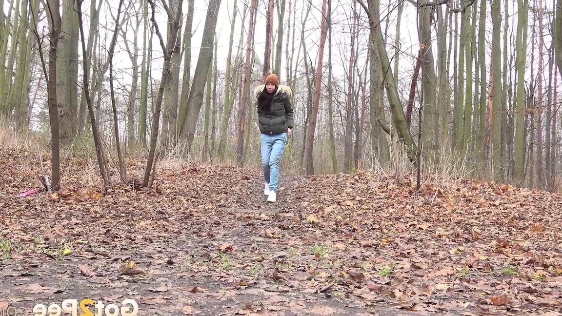 15P Dark-haired girl squats for a pee on leaf covered ground on a chilly day