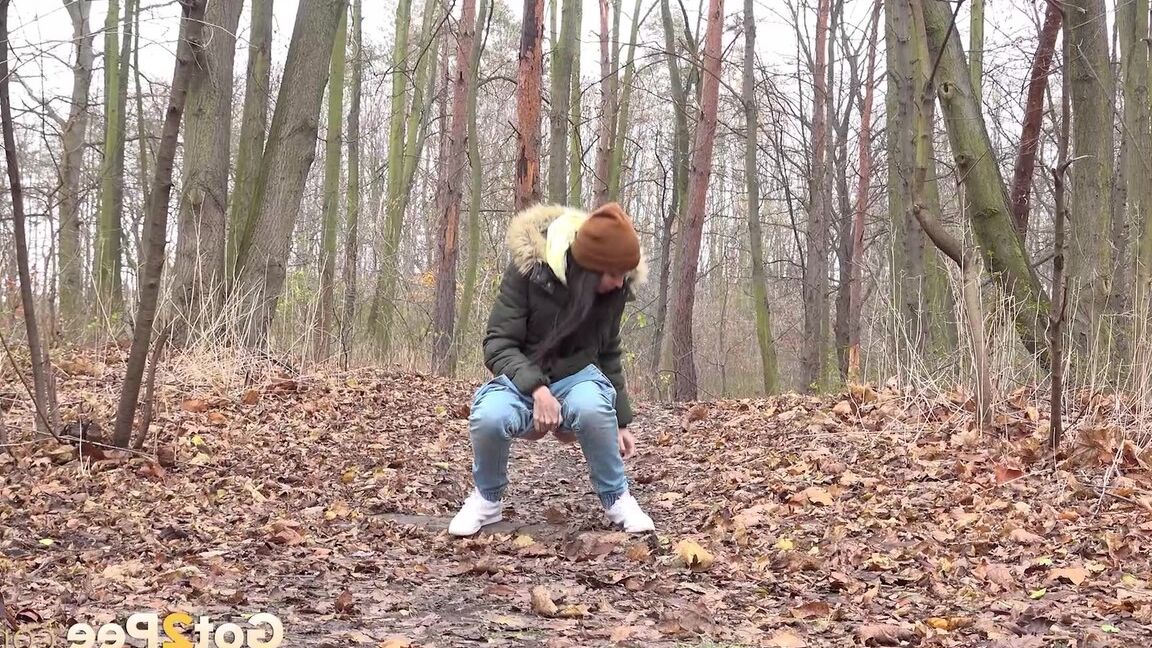 15P Dark-haired girl squats for a pee on leaf covered ground on a chilly day